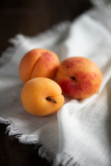 three orange apricots with white cloth on dark wooden table, farmers market fruit on towel, group of fresh fruit on table, orange fruit
