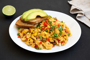 Homemade southwestern egg scramble with toast on a white plate on a black surface, low angle view. Close-up.