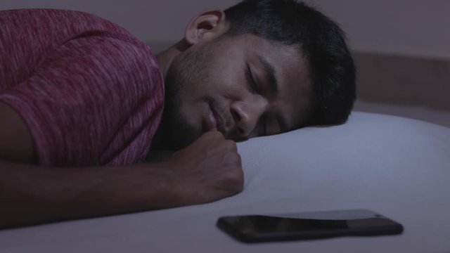 Concept showing of irregular sleep or sleep deprivation caused due to mobile phone, young adult got the message while sleeping causing disturbance and affects the sleep and health.