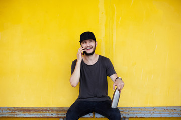 Happy guy is sitting on yellow background with steel thermo bottle in hand and talking on...