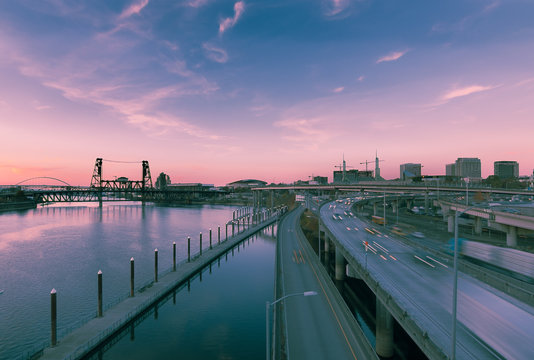 Long exposure of the Portland skyline looking north from the Burnside Bridge. Reflections on the Willamette and traffic blurred on I-5. Pink clouds. Space for copy.
