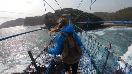 PoV action camera - funny woman invite to go on suspension bridge above ocean waves in Timang beach, Java island, Indonesia