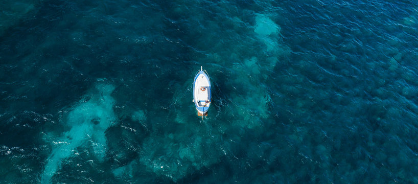 View from above, stunning aerial view of a beautiful fishing boat with a fisherman on board sailing on a blue sea. Amalfi coast, Italy