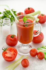 Tomato juice is poured into a transparent glass with parsley and herring, on a white background with cherry tomatoes, lit by sunlight