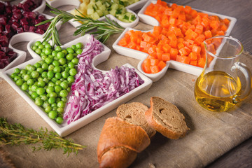 Delicious fresh pieces of vegetables of carrots, cucumber, potatoes, beets and peas close-up with fresh onion and olive oil on a bag cloth on a rustic gray table.