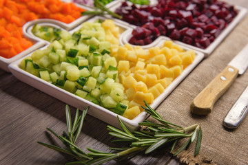 Delicious fresh pieces of vegetables of carrots, cucumber, potatoes, beets and peas close-up with fresh onion and olive oil on a bag cloth on a rustic gray table.