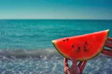 Fototapeta na wymiar Watermelon, juicy, red slice in the hands of a woman against the background of the ocean, in the rays of sunlight. Diet of tropical fruits.