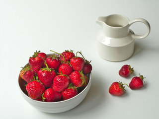 Fresh picked delicious strawberries in a white bowl with creamer on white table.