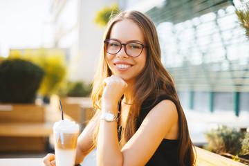 Photo of fashionable girl, sitting at terace and drinking ice coffee