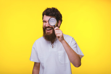 Photo of bearded guy investigating with magnifying glass, over yellow background