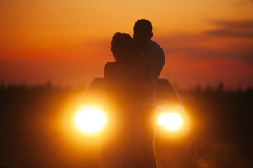 Fototapeta premium Silhouette of couple hugging in a field, on car lights in evening