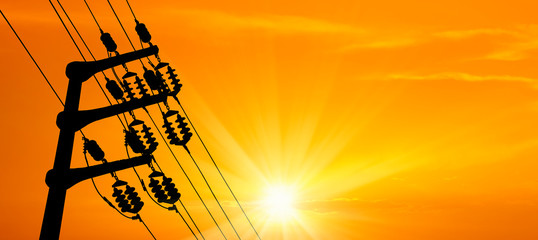 close up electricity power line tower over orange color sunset sky with shining sun
