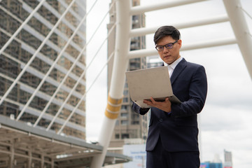 Fototapeta premium asian businessman standing outdoor using laptop computer