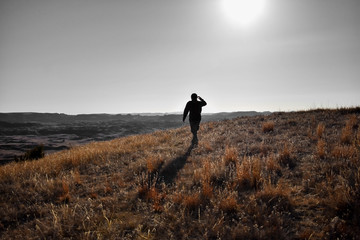 A silhouette of a person walking through rolling hills covered in green and yellow golden grass....