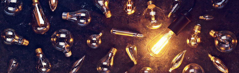 Vintage old light bulb glowing yellow on rough dark background surrounded by burnt out bulbs. Idea,...