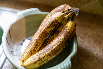 Bunch of very ripe bananas in serving bowl on counter