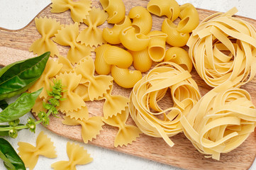 Different types of Italian pasta and fresh basil on wooden cutting board