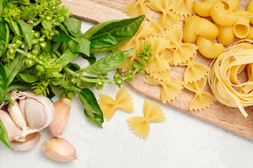 Different types of Italian pasta, fresh basil and garlic on wooden cutting board