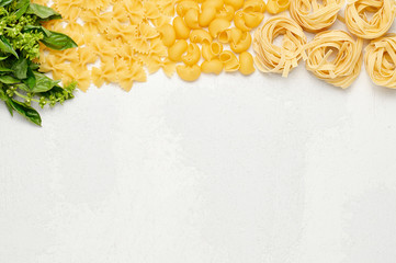 Different types of Italian pasta and fresh basil. Farfalle, Pipe rigate and Fettuccine on light grey background
