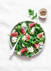 Figs, goat cheese, arugula salad on light background, top view. Delicious breakfast, snack, appetizer, tapas