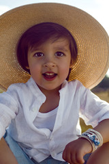 baby boy in straw hat and blue pants sitting on a haystack in a field