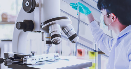 Young Asian male scientist looking at tube for research test. Double exposure with microscope and...