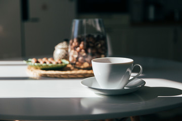 Macadamia nuts in a bowl and cup of tea or coffee stand in the kitchen table, hard morning light