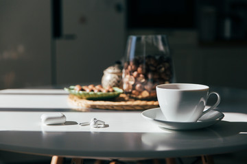 Macadamia nuts in a bowl, cup of tea or coffee and earphones lay in the kitchen table, hard morning light