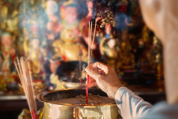 Faith and religious. .Man hand holding incenses  sticking  in  burner  at chinese shrine with bokeh...