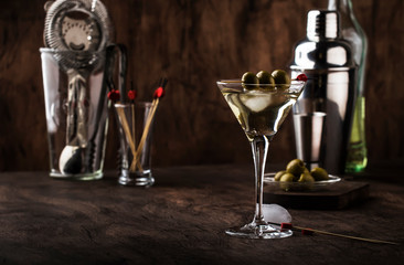 Martini vodka cocktail, with dry vermouth, vodka and green olives, bar tools, vintage wood counter, selective focus