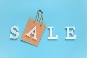 Text SALE from white volume letters and paper shopping bag on blue background. Top view Flat lay Copy space Concept discount. Creative template for your text, design, ad or advertisement