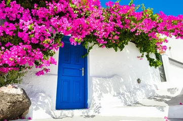 Wandaufkleber Weiße kykladische Architektur mit blauer Tür und rosa Blüten von Bougainvillea auf der Insel Santorini, Griechenland. © smallredgirl