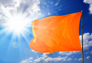 Conceptual image of waving blank orange flag over sunny blue sky