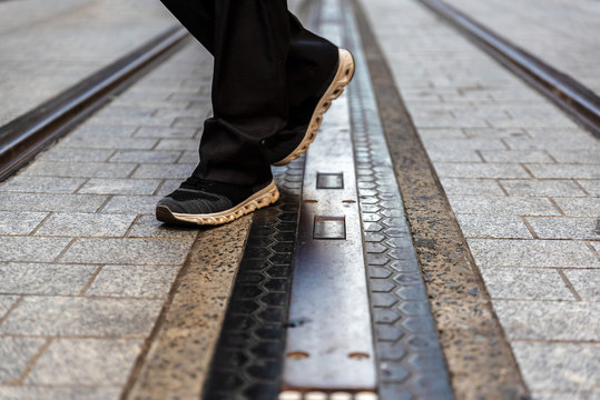 Man with black sneakers walking across light rail train tracks 