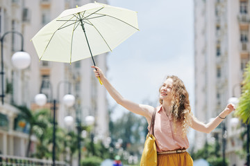 Pretty curly young woman using umbrella to protect herself from shining sun