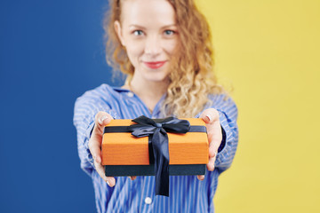 Pretty smiling young woman giving you present with a big deep blue bow