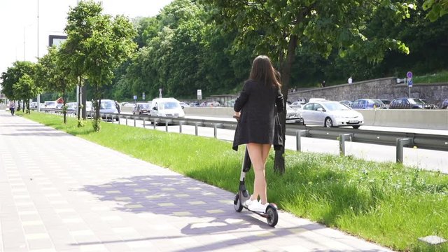 Slow motion.  Modern girl riding electric scooter in city area. Steady shot, back view