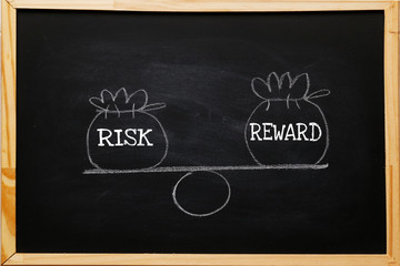 Write symbol Risk and reward bags on a basic balance scale in equal position on blackboard. depicts...