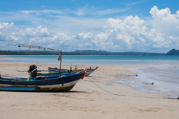 Side view of a wooden fishing boat on tropical beach with white sand and blue sky