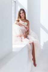 Elegant bride in wedding white dress sitting on window.