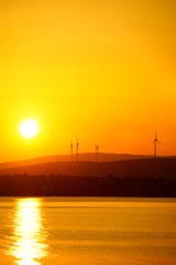silhouetted windmills on hill over orange colored sunrise sky