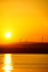 Fototapeta na wymiar silhouetted windmills on hill over orange colored sunrise sky