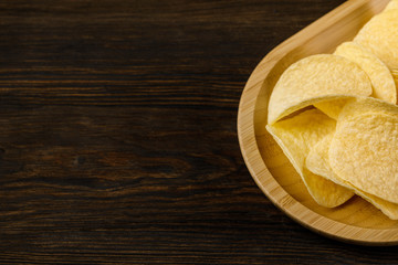 Salty delicious potato chips on wood background. top view