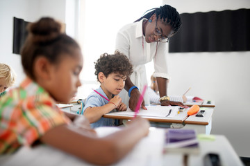Curly boy listening to African-American teacher wearing glasses