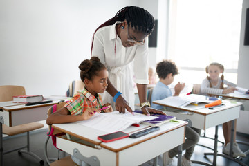 Teacher standing near little girl and reading for her