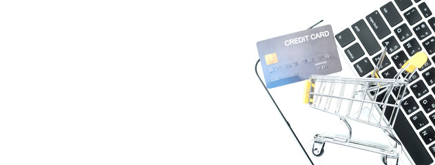 Online shopping. Bank card nearby a laptop and mini shopping cart on white background top view.-panoramic banner.