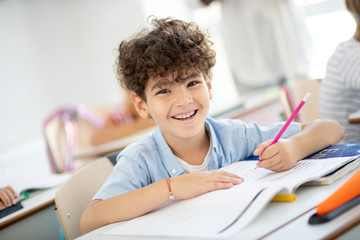 Cheerful curly boy feeling good while enjoying the lesson
