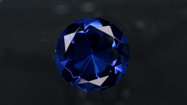 Rotation of a large blue rhinestone on a black background. With space for design, text place.