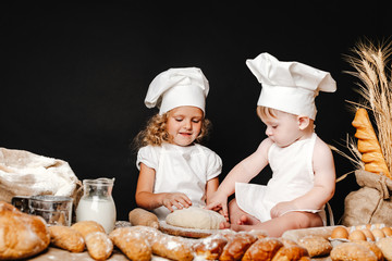 Little girl with baby in aprons on table with bread loaves making fresh dough and having fun