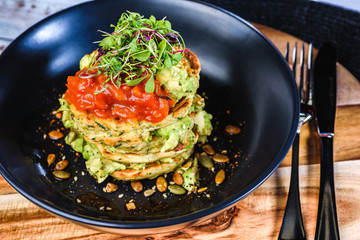 A dish of vegetable patties, Halloumi and Avocado, stacked up on a dark blue plate.